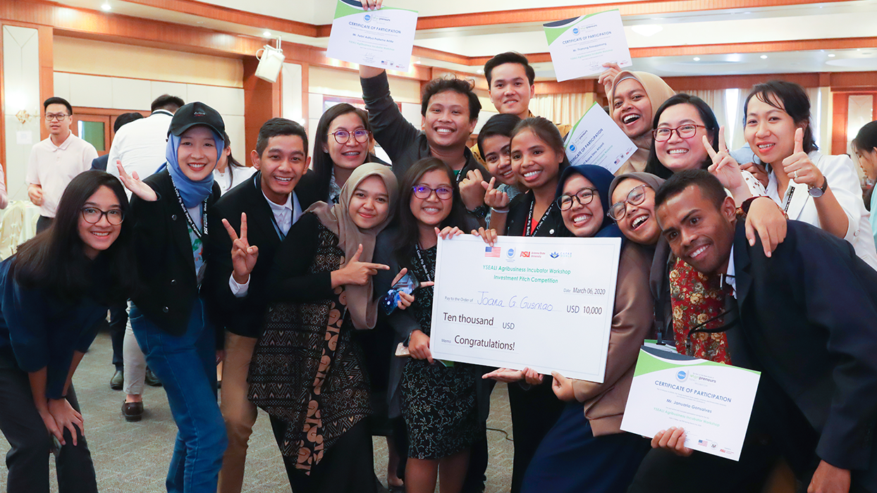 A group of smiling people holding a large check and certificates indoors.