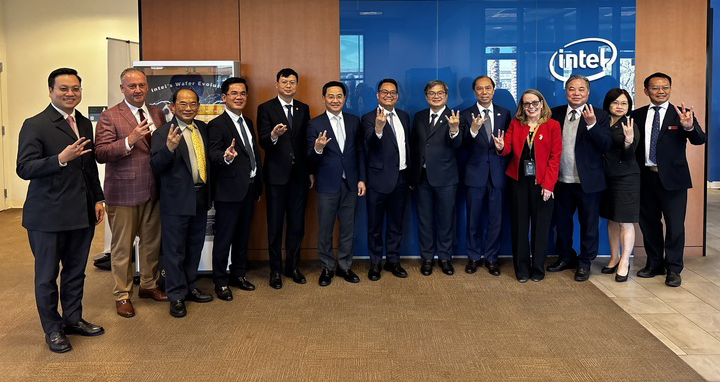 A group of 14 people in formal attire pose in front of a blue wall with the Intel logo.