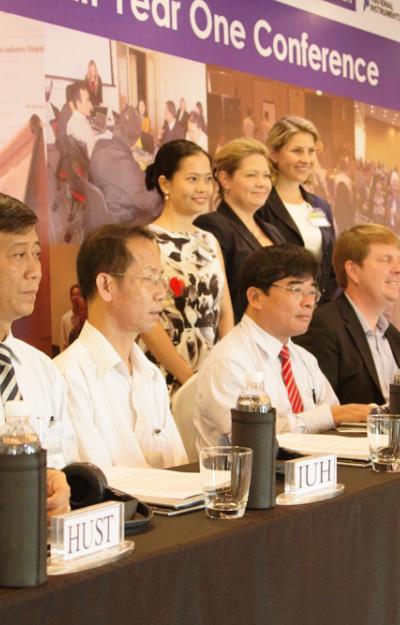 A group sitting and standing at a conference, with a banner reading "Year One Conference" above them.