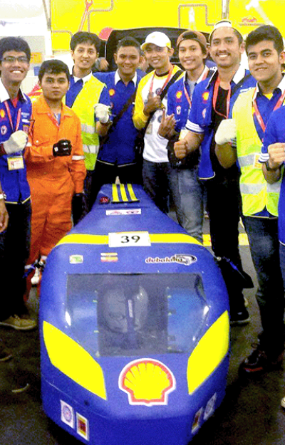 A group of young people in blue uniforms and safety vests pose around a blue and yellow vehicle with a Shell logo.