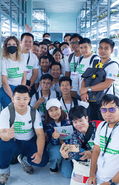 Mekong-U.S. Partnership Young Scientist Program—A group of people posing in a laboratory aisle filled with shelves of glass bottles containing plants.