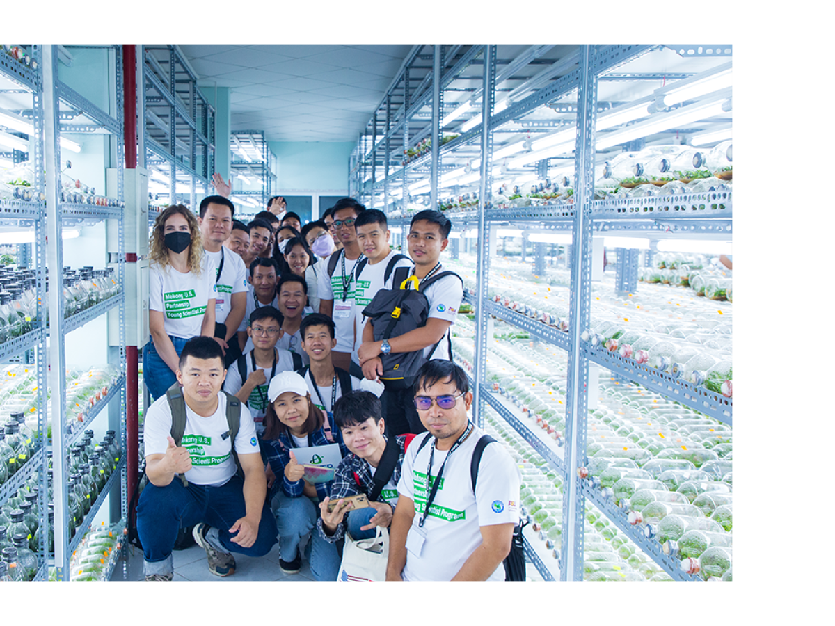 A group of people in a lab with shelves of plant containers.