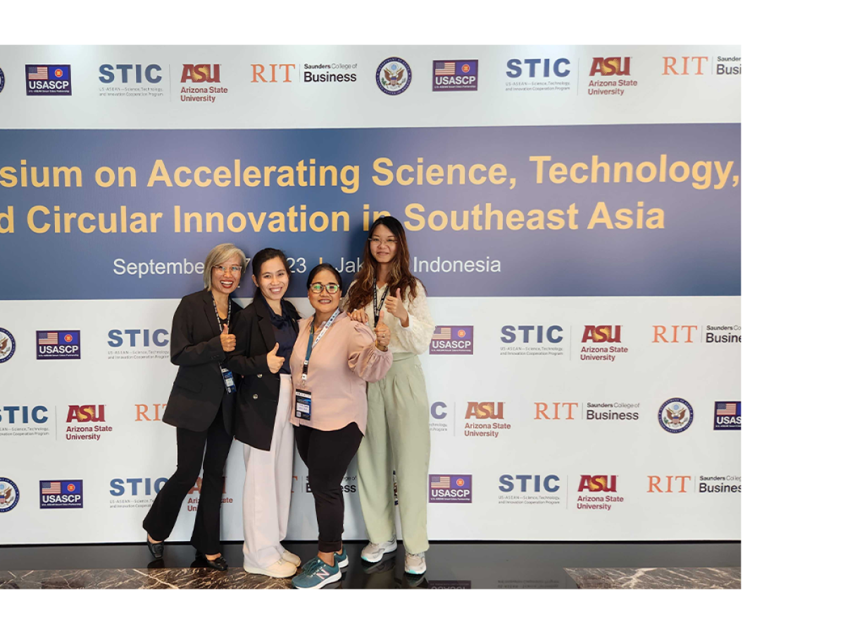 Four people stand smiling in front of a symposium banner featuring multiple logos and event details.
