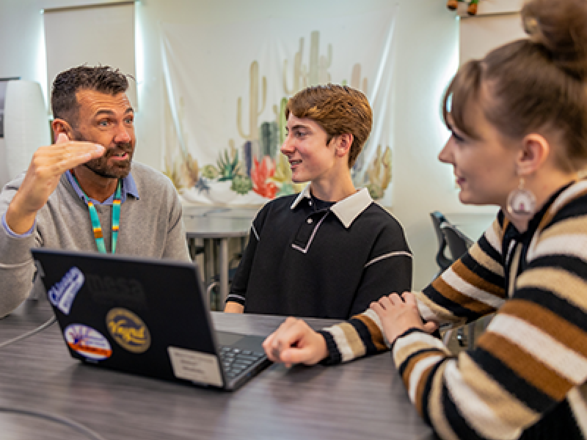 Three people sitting at a table having a discussion with a laptop displaying stickers.