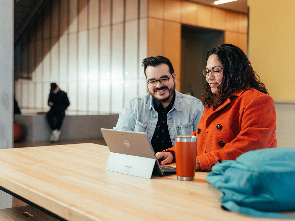 Two people sitting at a table working on a laptop in a modern indoor space.