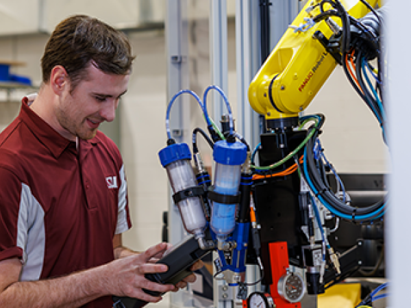 Man operating a yellow industrial robotic arm with a control device.